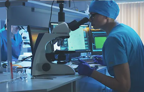 Researcher in blue scrubs using microscope